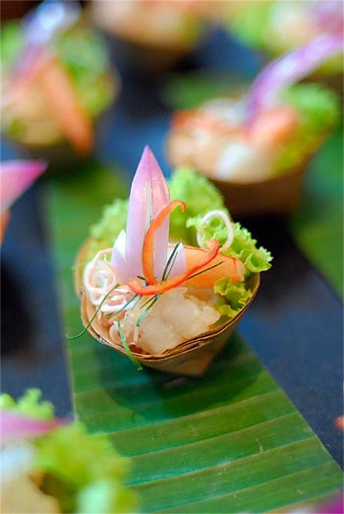 A pretty, small morsel of colorful food sits on a green leaf.