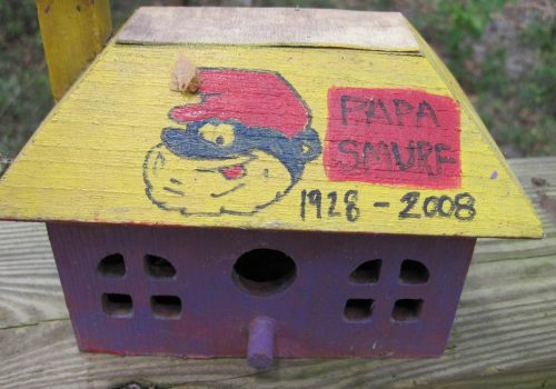 Some of the birdhouses on Birdhouse Canal are entirely handmade while others are store-bought and then decorated with artificial or natural items of personal significance. This homemade birdhouse is a memorial to a person nicknamed “Papa Smurf.”