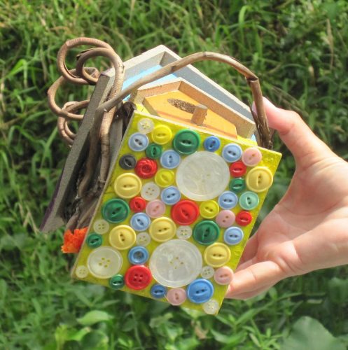 The public display of these birdhouses is a very personal and emotional undertaking. Intimate items from daily life are often attached to convey the individuality of each person being memorialized. This birdhouse is ornamented with buttons glued to its base.