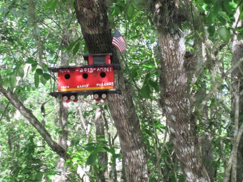 Most birdhouses memorialize family members or friends who are recently deceased. A birdhouse in the form of a train car (with an appended U.S. flag) honors a deceased child by noting her “freckles” and, presumably, some of her favorite things in life: “coco” and “candy.”
