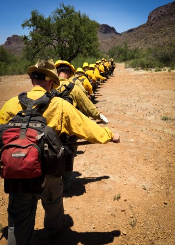 Inmate firefighters - This crew walks toward the edge of a fire that burned 100 acres in the span of an hour before they arrived. The fire burned in Arizona’s scorching mid-June heat, with the outdoor temperature climbing above 120 degrees Fahrenheit and increasing to 140 F near the fire itself. Each firefighter carries a 50-pound pack on his back, and some carry an extra 50 pounds in the form of chainsaws or water bags, whose contents are used to douse the flames. Mentally preparing for eight hours on the line, crews create a militaristic straight-line formation and yell “moving!” one at a time as they walk toward the heat.