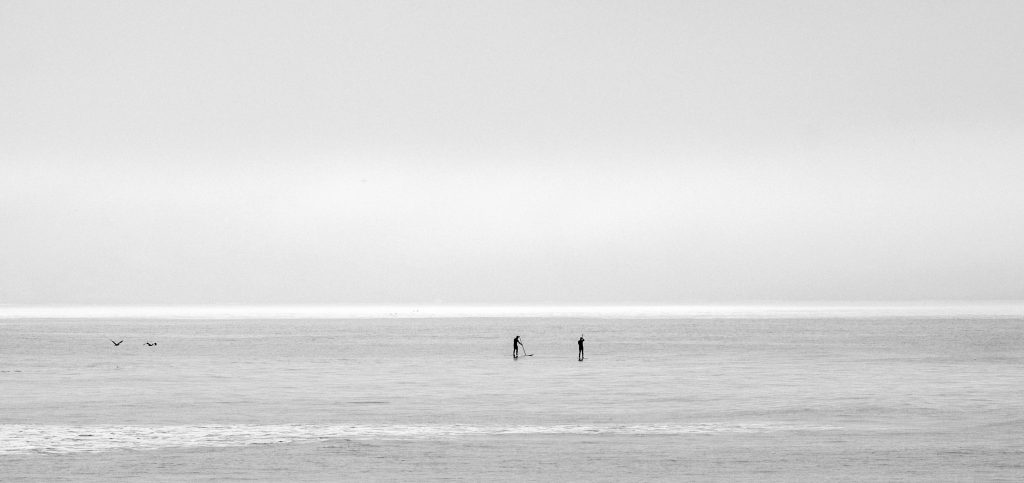A gray ocean fades into a gray sky, with a few swimmers barely visible in the distance.