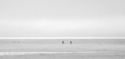 A gray ocean fades into a gray sky, with a few swimmers barely visible in the distance.