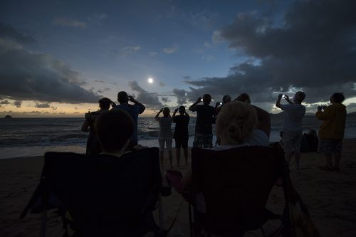 A small crowd stands in half-darkness, watching an eclipse.