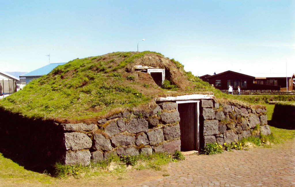 A squat stone building is covered with a grass roof.