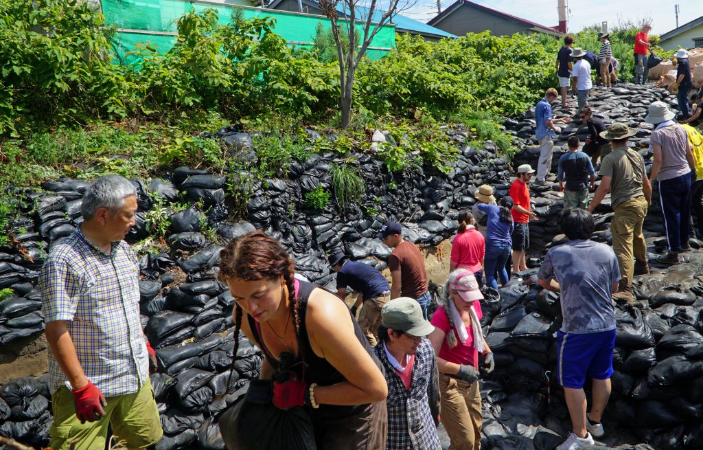 On Rebun Island, off the coast of Hokkaido, Hirofumi Kato, left, Zoe Eddy, foreground, and volunteers pile sandbags on the Hamanaka II archaeological site, where they will stay until the dig continues the following year.