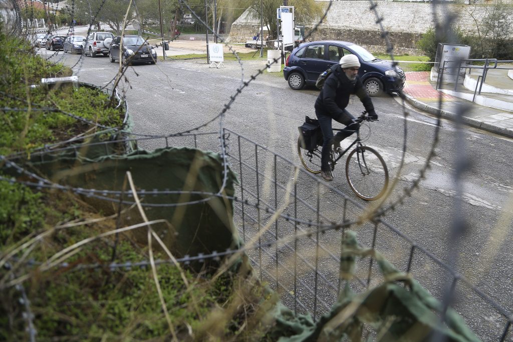 A person rides a bike next to a barbed wire fence.