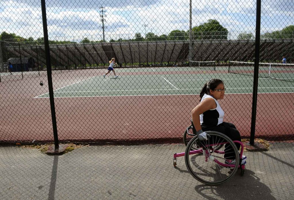 A high school freshman who has spina bifida participates on the varsity tennis team through the aid of a wheelchair.