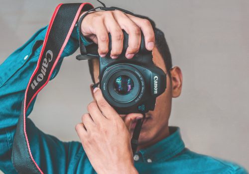 A photo shows a person holding a camera in front of their face to take a photo.