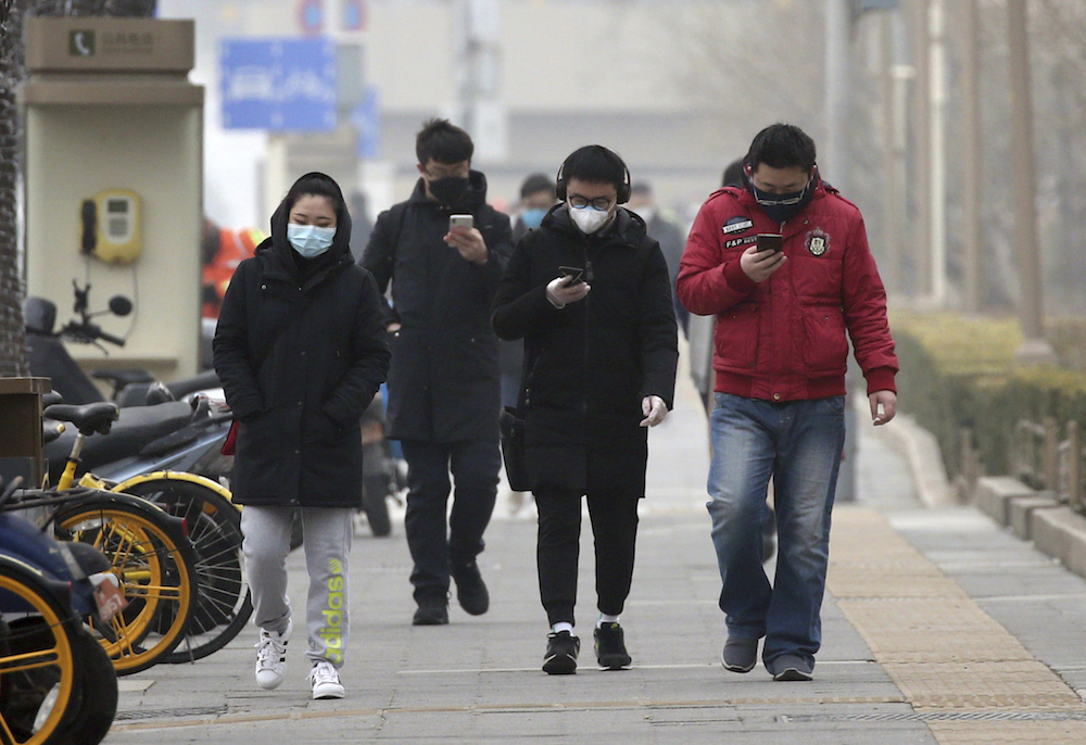 People with coats and face masks on walk down a gray sidewalk.