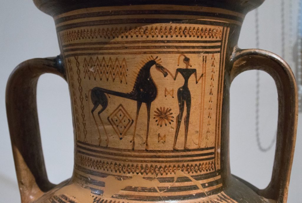 A piece of tan pottery shows a black abstract drawing that appears to be a horse and a woman.