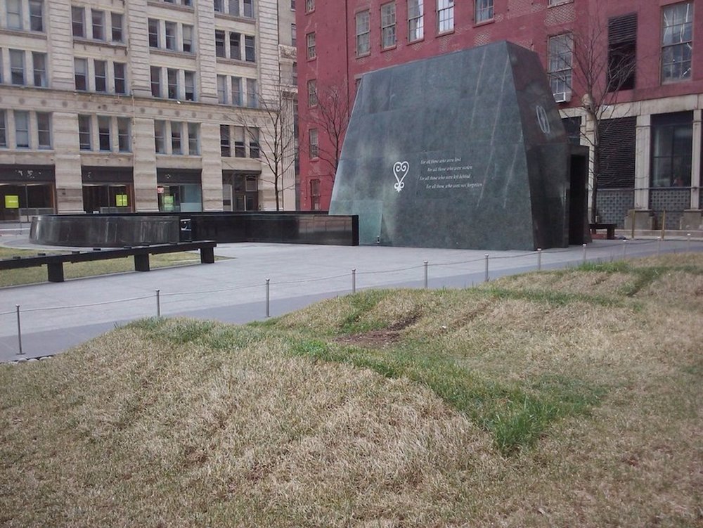 A tall stone sits in the middle of a public urban park.