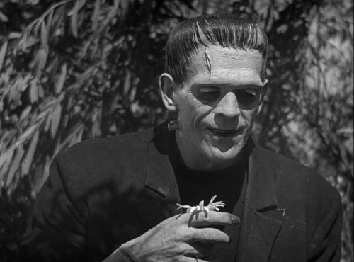 A black and white still image from a film shows Frankenstein with a bug perched on his hand.