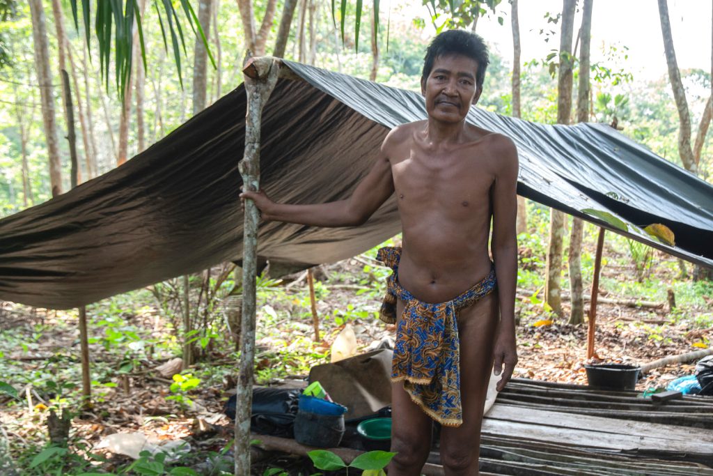 Orang Rimba covid-19 - An Orang Rimba man named Nyeruduk stands in front of a tent on a rubber plantation in Sumatra.