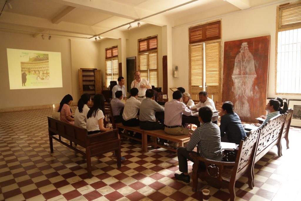 A person speaks to a group of people in a large, well-lit room.