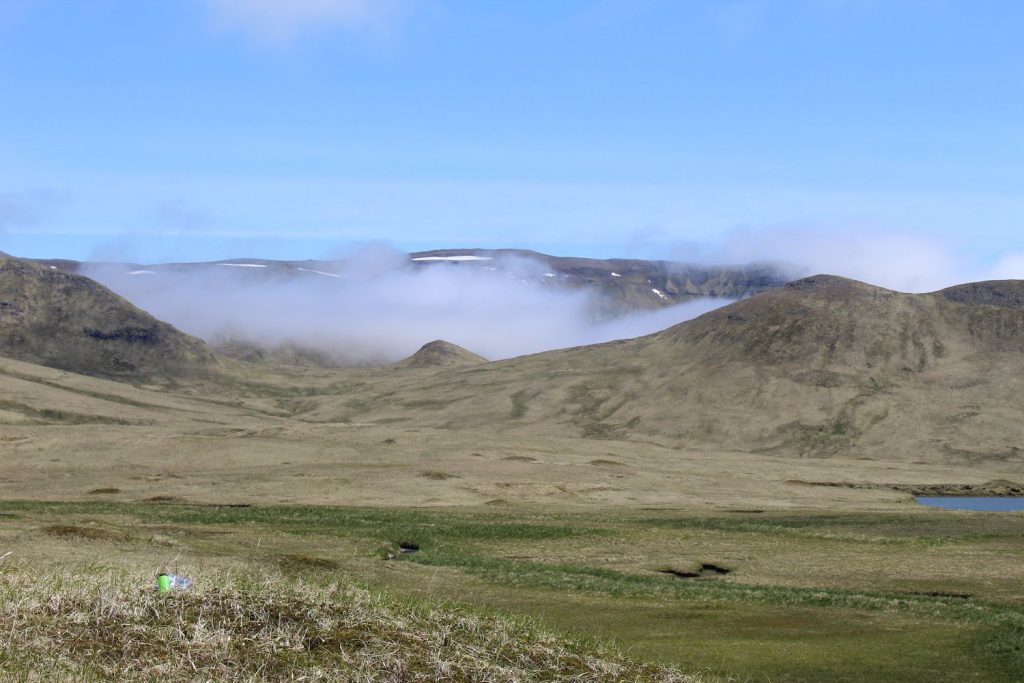 A landscape image shows clouds sitting low between hilltops and an open grassy plain.