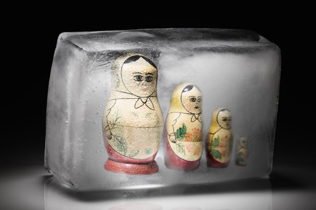 Four painted Russian dolls of different sizes lined up from largest to smallest frozen in a block of ice.