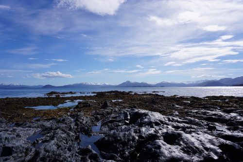 A landscape image shows a blue sky with clouds over rocks leading out to water and mountains in the distance.