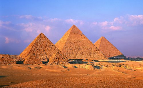 Three pyramids are shown in warm light against a blue sky with pink clouds.