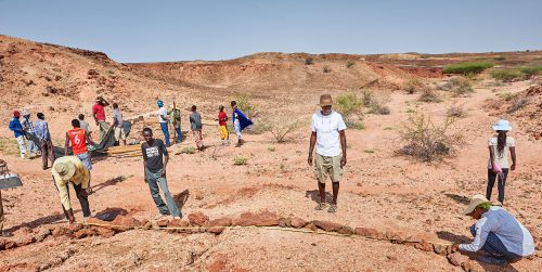 A group of people stand in a bright, dry valley measuring the ground and surveying the land around them.