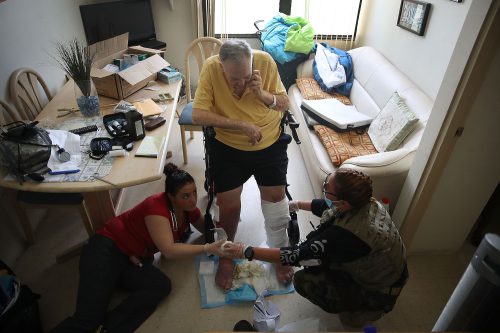 A man in an assisted living facility has his legs bandaged by two health care professionals as they prepare to evacuate him in the aftermath of Hurricane Maria.