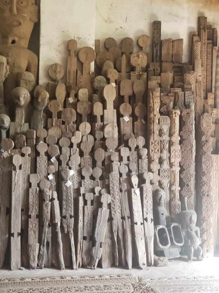 A collection of tall, thin wooden statues of different heights rests against a wall.
