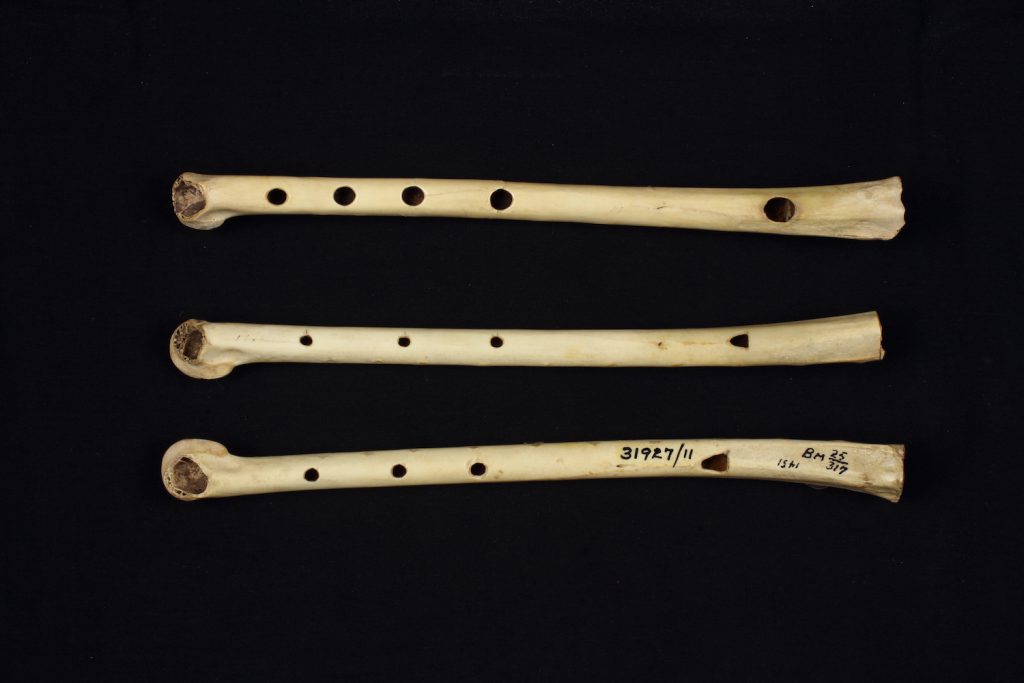 Three short flutes made of bone with holes in them have been placed horizontally against a black background.