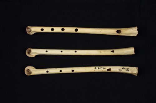 Three short flutes made of bone with holes in them have been placed horizontally against a black background.