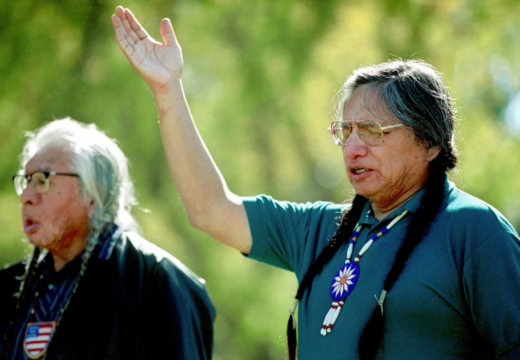 Two men with long braids and beaded necklaces pray.