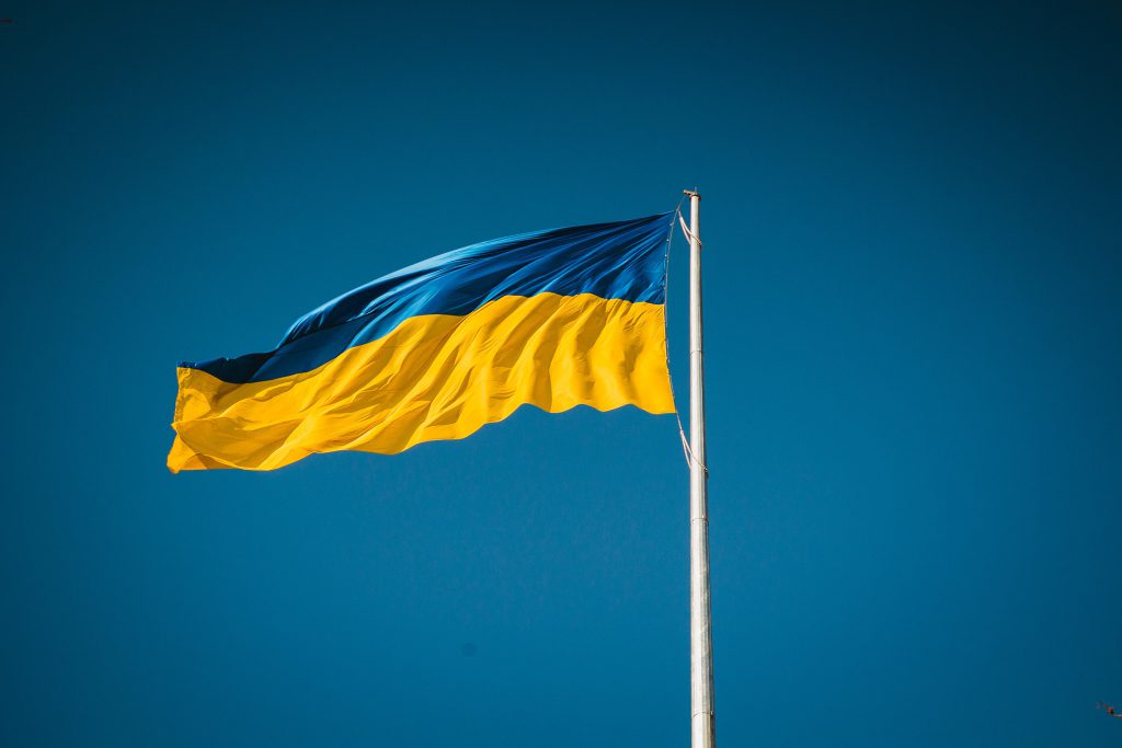 The flag of Ukraine, a blue stripe with a yellow stripe below, waves in front of a blue sky.