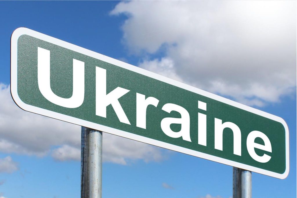 A sign with the word Ukraine stands alone before a cloud-filled sky.
