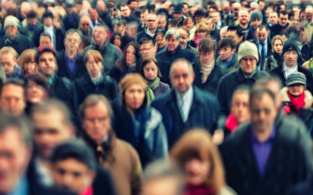 A crowd of people with blurred faces walk in the same direction wearing coats and hats.