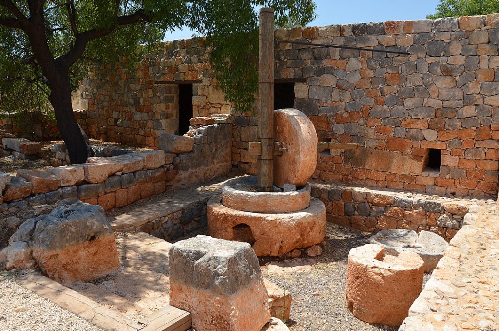 Reddish-brown stone cylinders sit in a square stone courtyard in front of a wall.