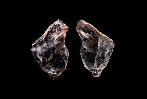 Two black and brown triangular stones face each other against a black background and are lit from above.