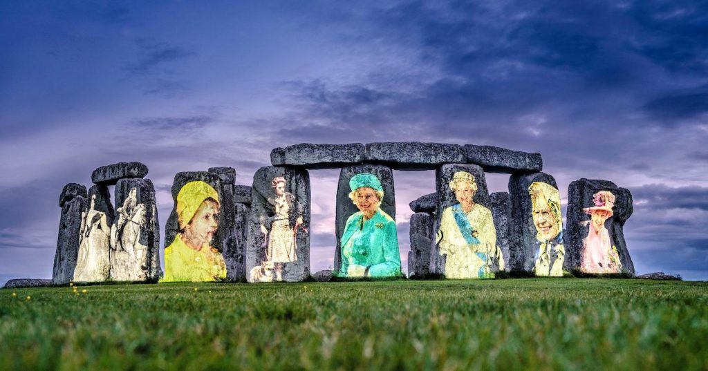 Ocho imágenes de la reina Isabel II en distintas edades aparecen en ocho monolitos de Stonehenge, con un cielo azul oscuro.