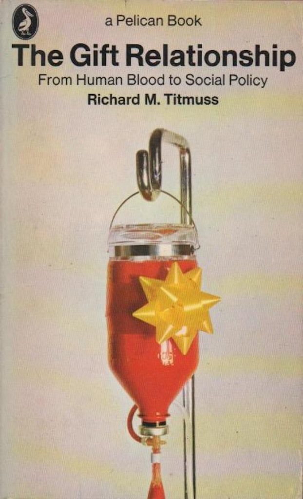 La cubierta de un libro de color canela muestra una bolsa de sangre roja con una cinta amarilla de regalo y un texto negro que dice: “Un libro de Pelican. La relación de los regalos: De la sangre humana a la política social. Richard M. Titmuss”.