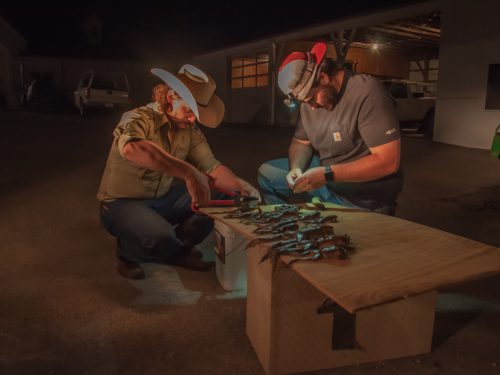 Two men squat next to a wooden board that holds frogs, using pliers and knives to take apart the carcasses.