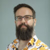 A man with a beard, glasses, and patterned shirt faces forward.
