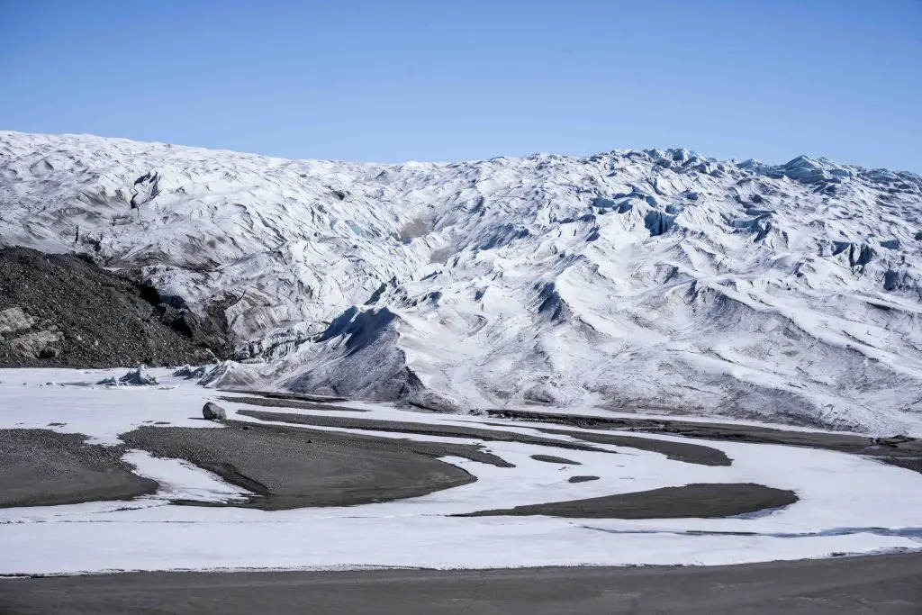 Uma fotografia apresenta uma paisagem rochosa branca com neve sob um céu azul claro.