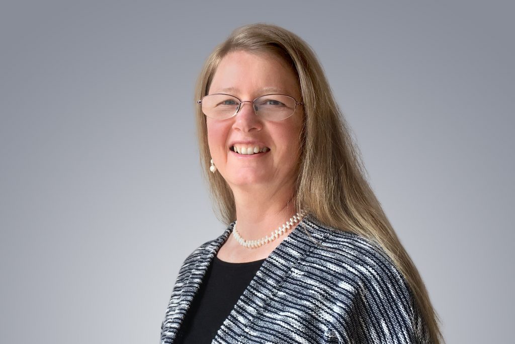 A woman with blond hair and glasses smiles warmly into the camera.
