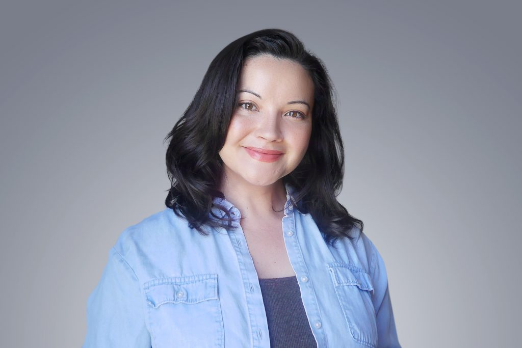 A woman with shoulder length black hair smiles warmly into the camera.