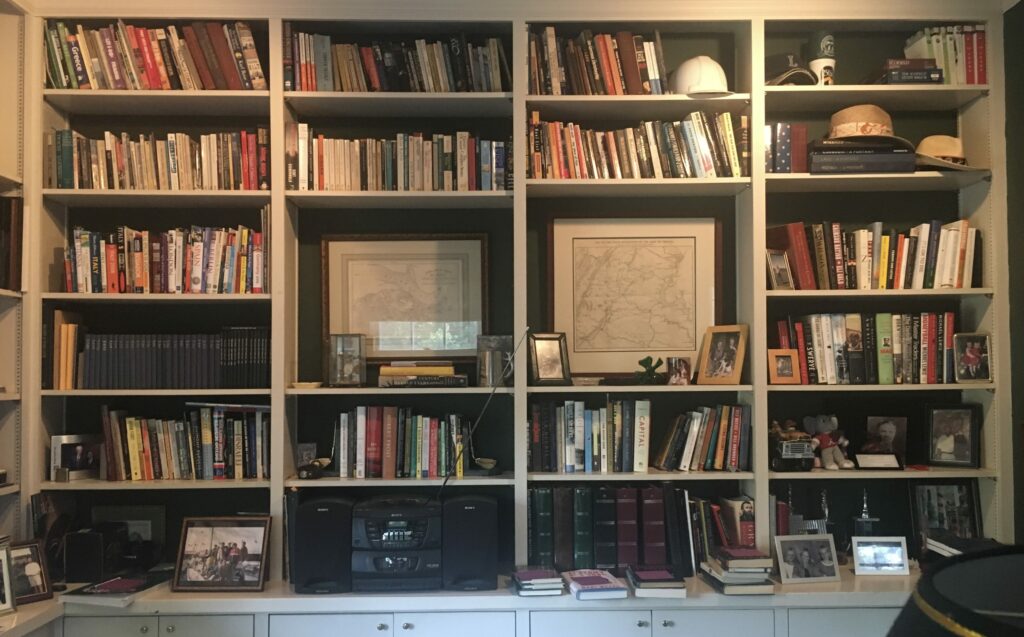 A large white bookcase is filled with books, photographs, framed degrees, electronics, and other family paraphernalia.