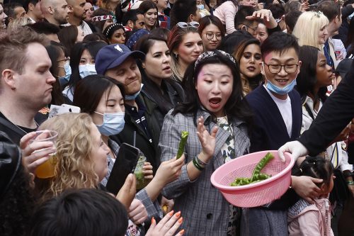A crowd of people gather, with those in the front row reaching out to take green peppers from a pink colander.