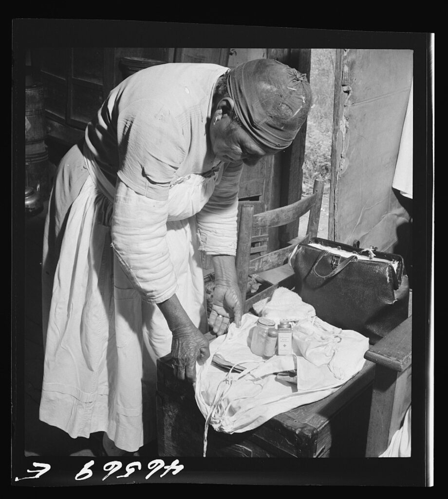 A black-and-white photo shows a woman wearing an apron bending over a cloth containing medicines in bottles.