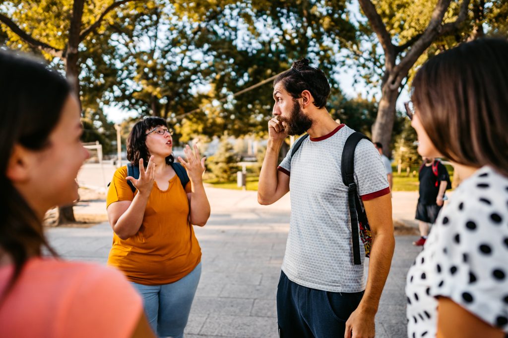 Personas sonrientes forman un círculo en el exterior, y algunas utilizan el lenguaje de señas.