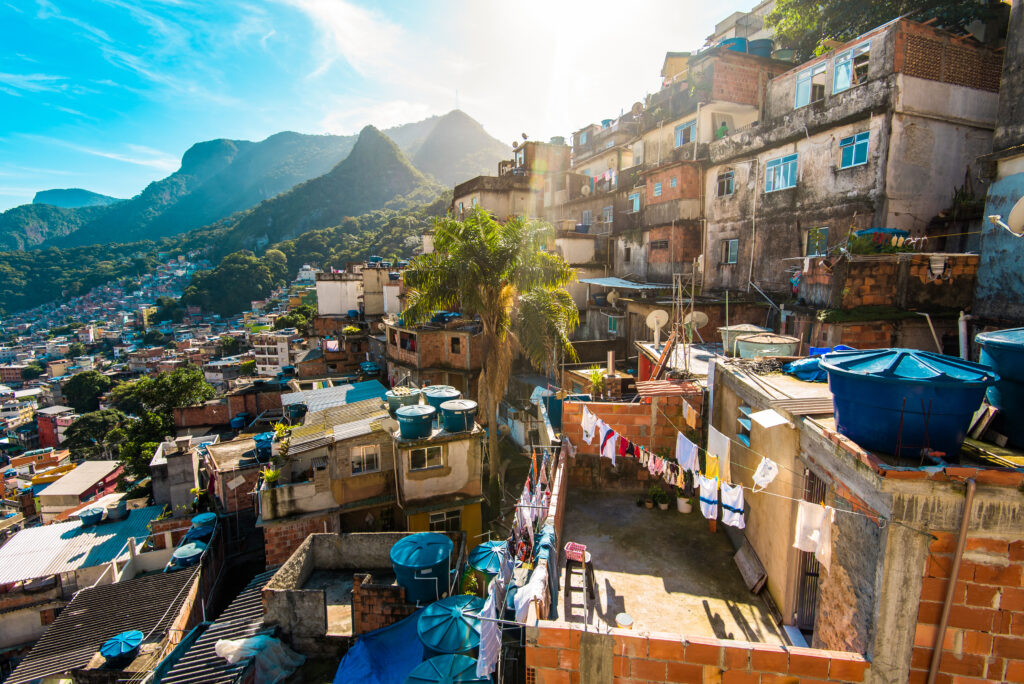 A landscape photo features dense buildings on a hillside under blue skies, with a mountain range in the background.