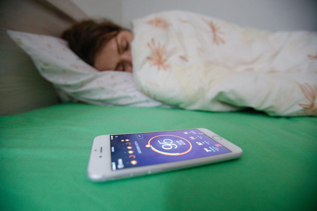 A person lies in bed next to a smartphone displaying numbers and symbols.