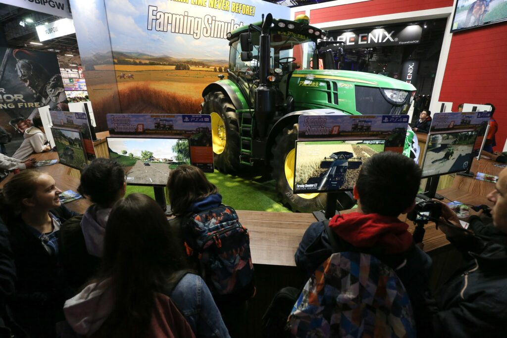 Children stand in front of video game displays and a large green tractor.