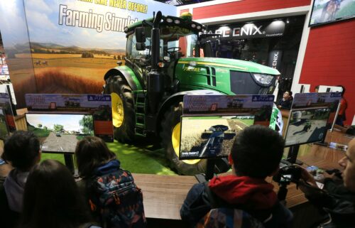 Children stand in front of video game displays and a large green tractor.