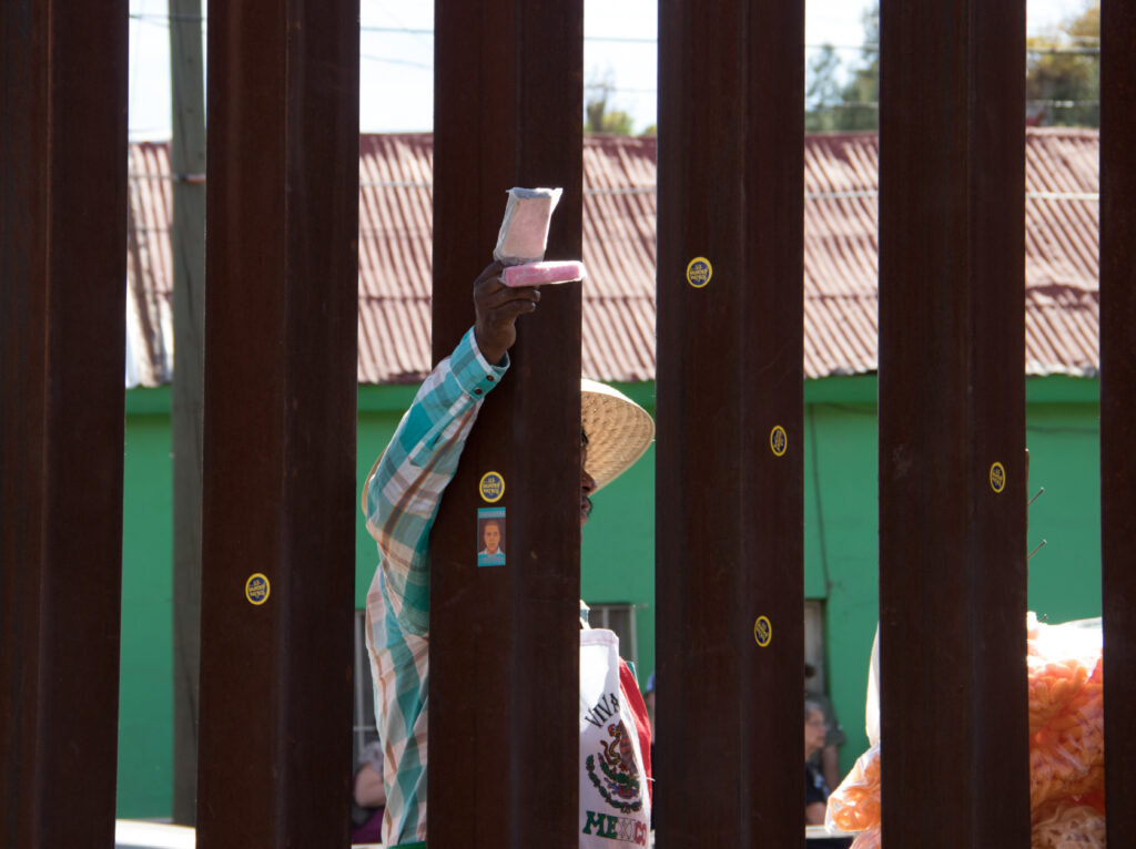 A person stands behind slats of a metal fence and reaches through to hold two small objects up on the other side.